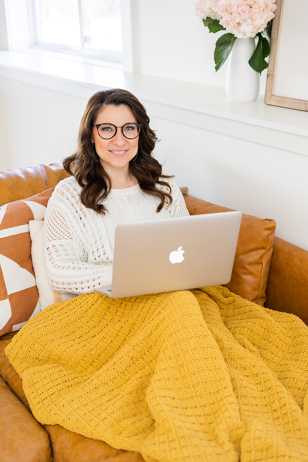 A business owner sitting on a couch with a laptop during a light and airy branding photography session in Rockville, Maryland. 